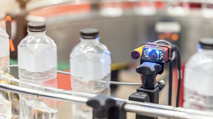 En sensor med digital skärm kontrollerar flaskor på ett rullband.